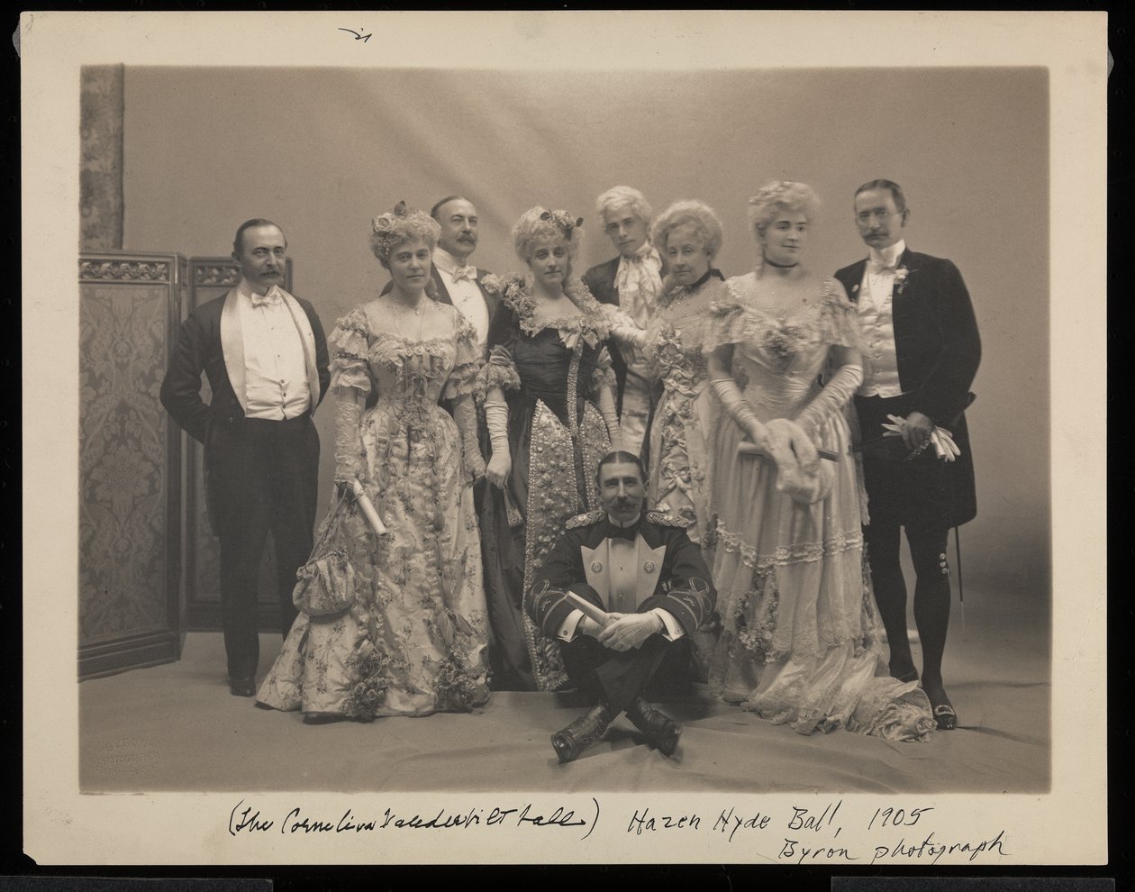 Portrett av fem menn (inkludert Coleman Drayton, August Belmont og Frank Hoppin sittende på gulvet) og fire kvinner (inkludert Mrs. Stuyvesant Fish) på James Hazen Hyde Ball, New York, 31. januar av Byron Company