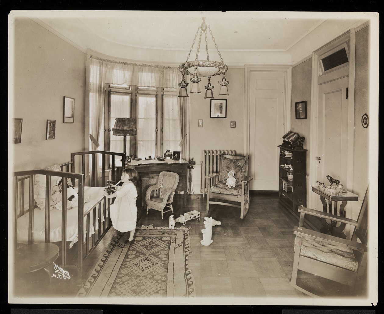 En jente som holder et stearinlys, klatrer opp i en barneseng, på et soverom i A.C. Cronin-residensen, 1915-16 (sølv gelatintrykk) av Byron Company