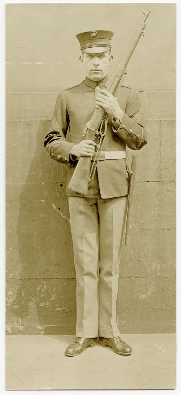 Uniformert soldat poserer for et bilde foran en betongmur av Carl Michel