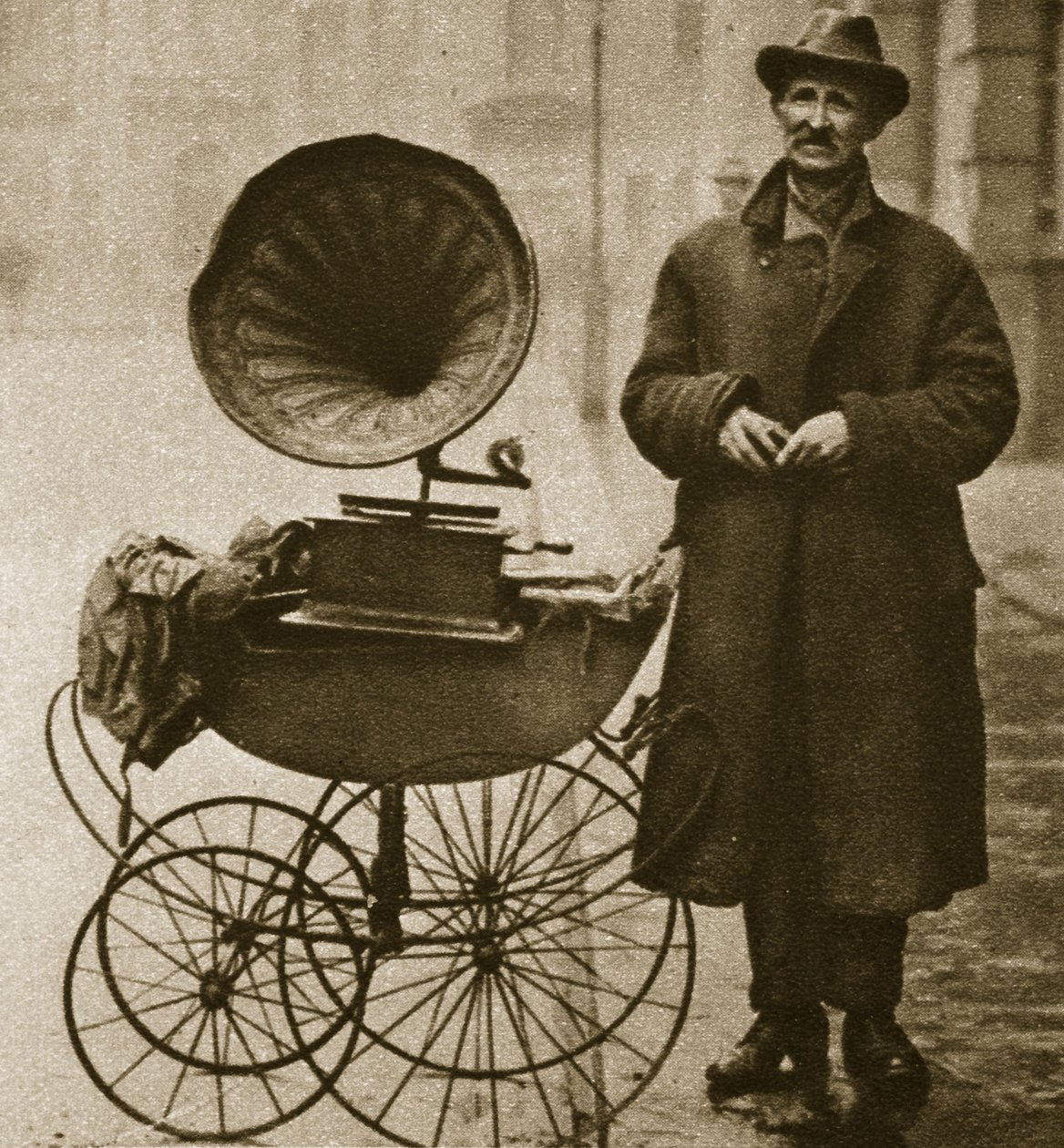 En gateselger underholder med en grammofon, fraktet i barnevogn (sepia-bilde) av English Photographer