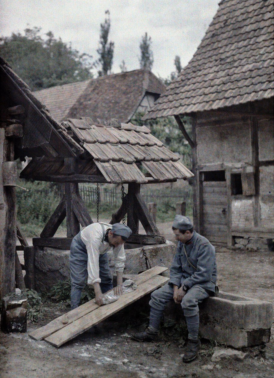 To franske soldater tar seg av klesvasken ved hjelp av brett satt opp på trauet til en fontene nær et gårdshus i byen Gildwiller, Department Haut-Rhin, Alsace, Frankrike, 21. juni 1917 (a av Paul Castelnau